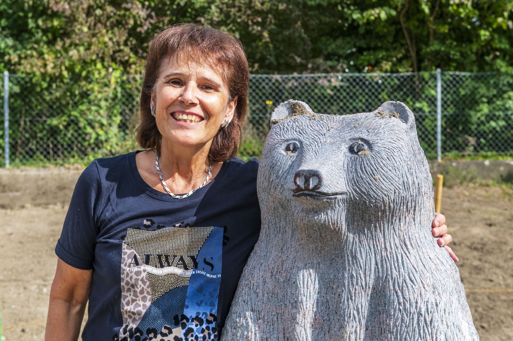 Eine Frau umarmt einen Bären aus Granit.